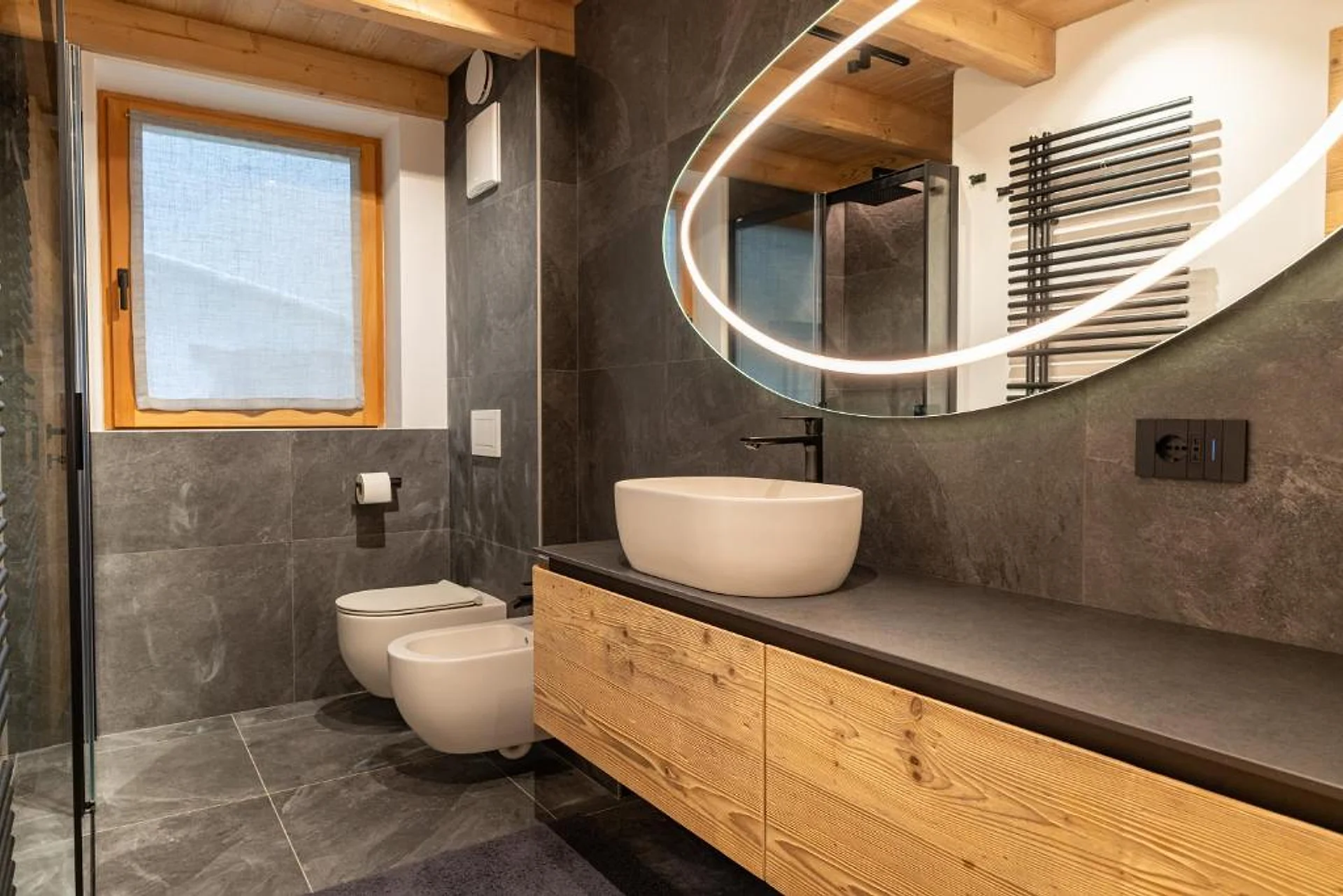 Bagno finito con mobile lavabo in legno, lavabo d'appoggio e specchio retroilluminato.